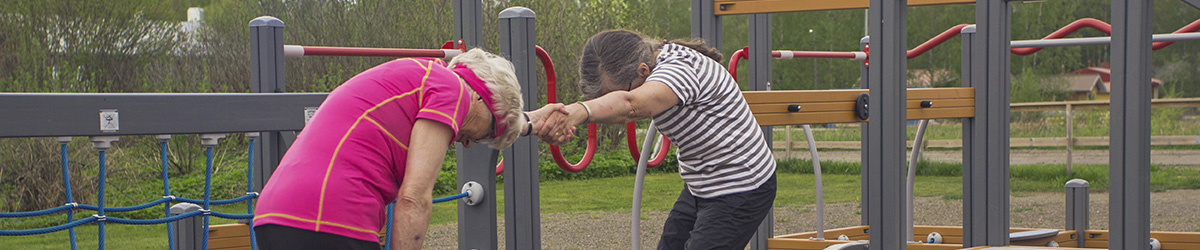 Seniorit venyttelevät yhdessä ulkona senioripuiston telineiden luona.