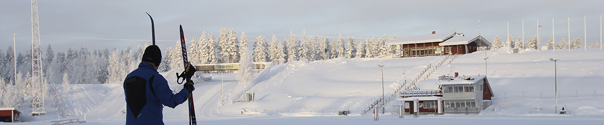 Mies pitelee suksiaan ja sauvojaan Pärnävaaran hiihtostadionin liepeillä katsellen lumista maisemaa.