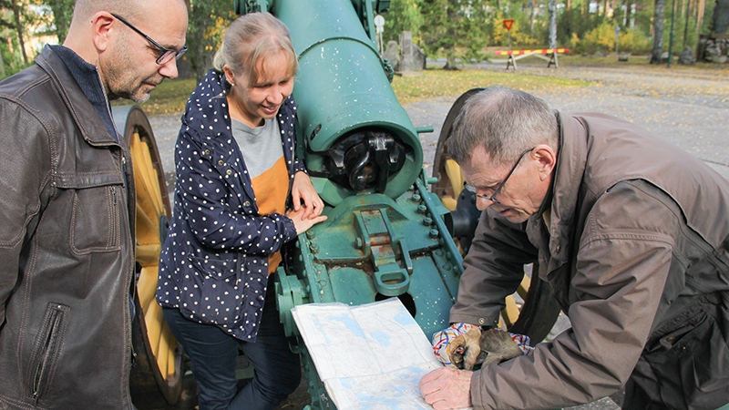 Veijo Wälkky kumartuu tutkimaan karttaa, Jyri Martikainen ja Outi Juurikainen katsovat.