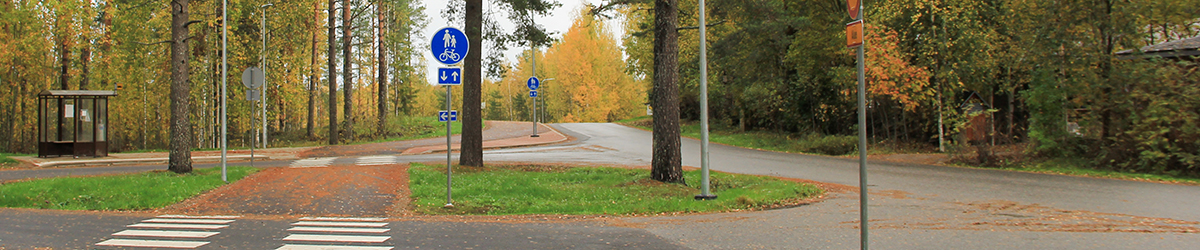 Kevyen liikenteen väylä ja autotie taajamassa, teiden vierustoilla mänty- ja lehtipuita.